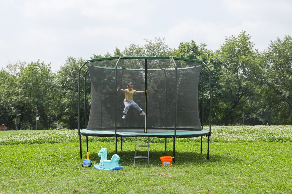 Child bouncing on 14ft enclosed trampoline in residential backyard - home entertainment solution